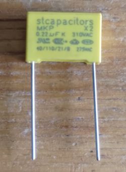 Żółty kondensator foliowy MKP X2 0,22 µF 310 VAC z dwoma wyprowadzeniami na drewnianym tle