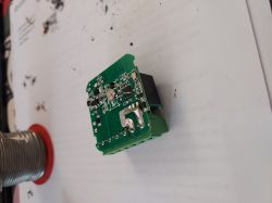 The image shows the back of a green circuit board with a soldered wire.