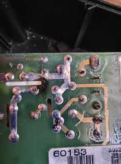 Spód płytki PCB z lutami, ścieżkami i śladami korozji oraz przypaleniem przy białym elemencie