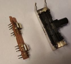 Rozłożony przełącznik suwakowy z widoczną płytką i elementami metalowymi na białym tle.