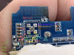 Close-up of a blue PCB held between fingers, with antenna trace and colored handwritten annotations