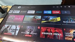 Ekran telewizora z interfejsem smart TV i kafelkami aplikacji oraz filmów na blacie