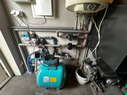 Hydrofor z niebieskim zbiornikiem i instalacją rur oraz zaworów na ścianie