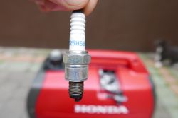 CR5HSB Spark Plug in Front of Honda Generator CR5HSB spark plug held in hand, with Honda generator in the background.