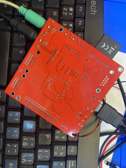 Red PCB on a black keyboard with several connected cables.