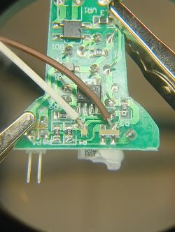 PCB close-up with soldered wires and surface-mounted components in metal clips
