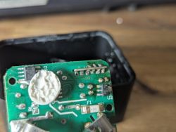 Close-up of the underside of a green PCB in a plug housing, with white compound and SMD parts