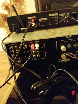 Zbliżenie na tylne panele urządzeń audio z podłączonymi kablami RCA i anteną.