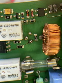 Zbliżenie na płytkę drukowaną z elementami elektronicznymi, w tym cewką, bezpiecznikiem szklanym i drobnymi komponentami SMD.
