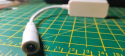 White cable with DC connector on a green cutting mat with a centimeter scale.