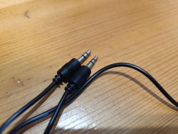 Dwa czarne przewody zakończone wtykami mini jack 3,5 mm leżące na drewnianym blacie.