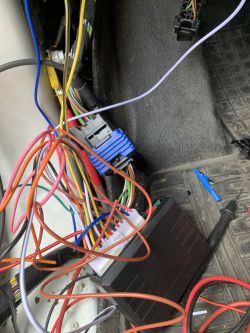 Zdjęcie przedstawia plątaninę kolorowych kabli w samochodzie, podłączonych do różnych wtyków i urządzenia.