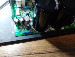 Widok zbliżeniowy płytki drukowanej wzmacniacza audio z widocznymi kondensatorami elektrolitycznymi i rezystorami mocy.