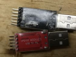 Two USB to TTL converter modules, CP2102 and an unmarked one, on a wooden surface