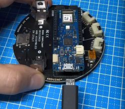 Zbliżenie na płytkę Arduino MKR WiFi 1010 połączoną z modułem MKR IoT Carrier, trzymaną ręką, z podłączonym kablem Micro USB.