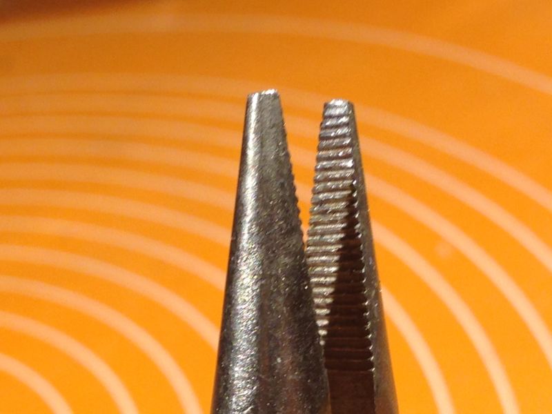 Zbliżenie na ząbkowane szczęki kombinerek na tle pomarańczowej powierzchni z białymi okręgami.