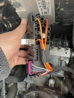 Close-up of a VAG fuse box with attached wires in a vehicle engine.