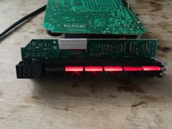 Panel sterujący i płytka drukowana programatora zmywarki z podświetlonymi przyciskami i wyświetlaczem LED na stole.