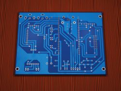 Bottom view of a blue PCB with vias and traces, placed on a red textured background.