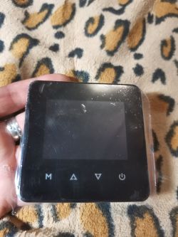 Black thermostat with a display, held in hand, against a patterned fabric background.