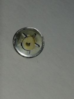 Mała metalowa część z otworem na środku, leżąca na białym tle.