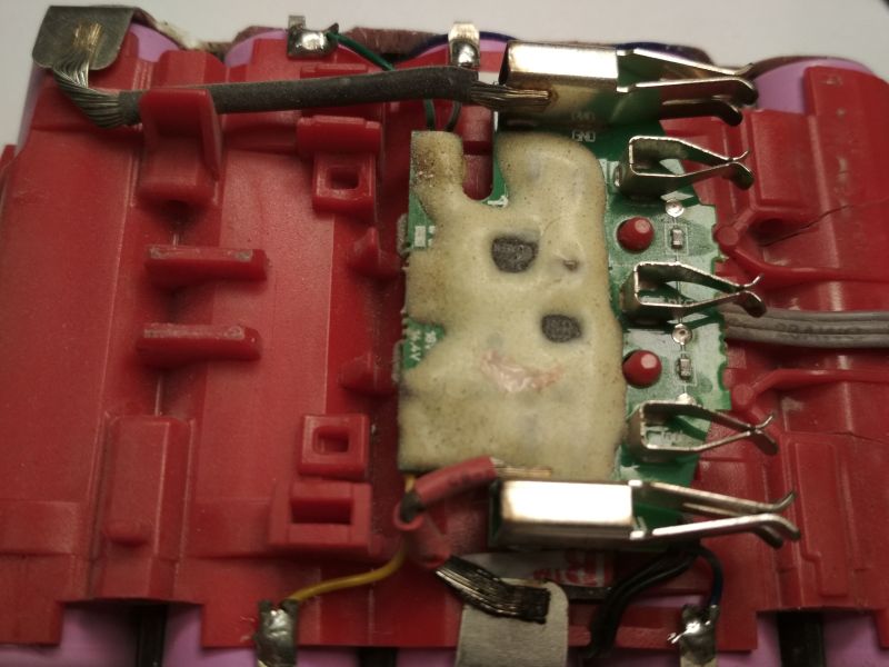 Widok wnętrza akumulatora Megatto 18V z płytką PCB i przewodami, zamontowanych na czerwonej obudowie.