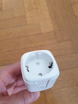 White smart plug held in hand against a wooden floor background