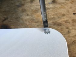 Unscrewing a spanner screw in the power strip casing with a spanner screwdriver on a white surface.