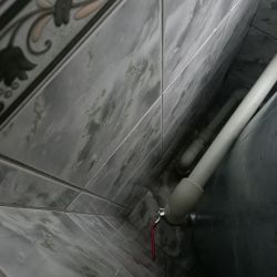 Zbliżenie na instalację hydrauliczną z rurami i zaworem, przy ścianie pokrytej kafelkami.