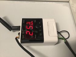 Electronic thermostat with a display showing 25 degrees Celsius, an antenna, and buttons.