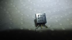 Nahaufnahme eines Transistors mit der Aufschrift DO34 MPF 102 auf weißem Hintergrund.