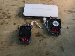 Powerbank podłączony do dwóch testerów obciążeniowych z wentylatorami i wyświetlaczami napięcia