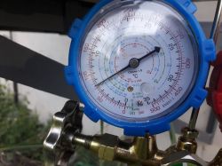 Manometr z niebieską obudową pokazujący ciśnienie gazu, podłączony do metalowej instalacji.