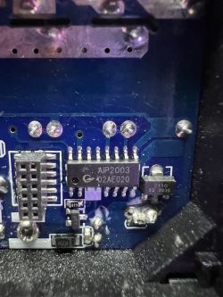 Close-up of an AIP2003 integrated circuit on a blue printed circuit board with various electronic components.