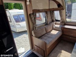 Interior of a caravan with a sofa, cabinets, and a view outside where another caravan is parked.