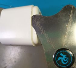 Measuring the edge of a white plastic part Close-up of a white plastic cylinder and a metal measuring tool with scale checking an edge