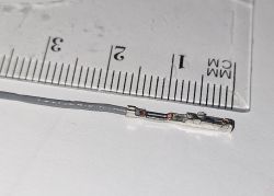 Metalowy pin z przewodem o długości około 16 mm obok linijki z podziałką w milimetrach