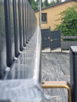 Zbliżenie na wygiętą stalową belkę bramy przesuwnej z widocznymi odchyleniami na całej długości.