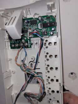 Zbliżenie na wewnętrzną część obudowy systemu domofonowego z widoczną płytką drukowaną i kolorowymi przewodami.