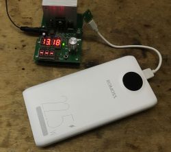 Powerbank Romoss podłączony do elektronicznego testera obciążenia na drewnianym blacie.