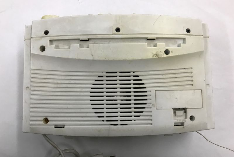 Bottom view of a white kitchen radio with a speaker grille and a battery compartment cover