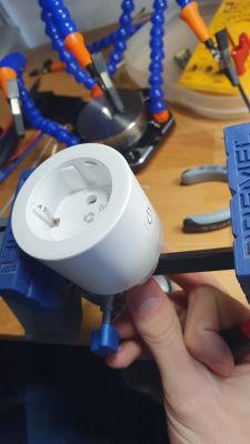 Person holding a white electrical plug clamped in a vice on a workbench.
