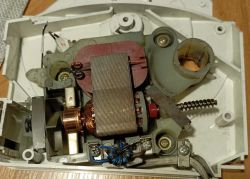 Widok wnętrza silnika elektrycznego z komutatorem, cewkami i sprężyną, umieszczony w plastikowej obudowie.