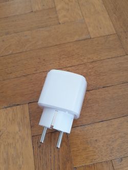 White smart plug lying on a wooden floor.