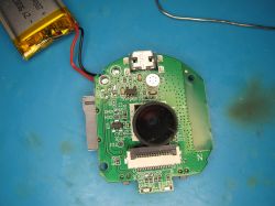 Camera Electronics with Connected Battery A circuit board with a mounted camera lens and a lithium-polymer battery on the left.
