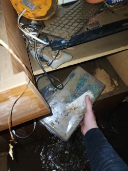 Hand holding flooded electronic equipment in a destroyed and flooded room.