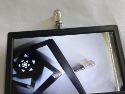 Small monitor with a black bezel shows a camera feed; a tiny bulb is visible above the bezel and on screen.