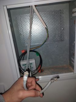 Wnętrze skrzynki teletechnicznej z kablami i dwiema końcówkami RJ45 trzymanymi w dłoni