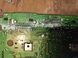 Zbliżenie na płytkę PCB z radia samochodowego Mitsubishi, z widocznymi ścieżkami i miejscem po wylutowaniu układu IC802.
