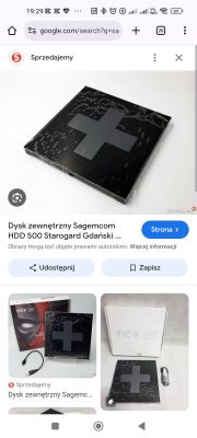 Czarny dysk zewnętrzny Sagemcom z dużym szarym krzyżem na obudowie, widok z góry.